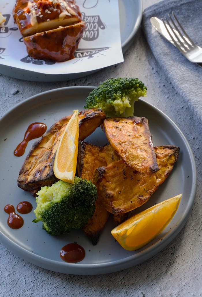 A plate of roasted sweet potatoes, broccoli, and oranges with sauce, perfect for healthy dining.