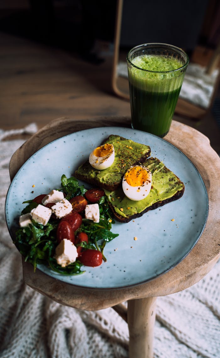 Delicious avocado toast with eggs and a refreshing green smoothie on a wooden table.